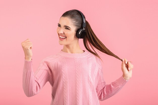 woman listening to music in wireless headphones wearing pink sweater smiling happy positive mood posing on pink