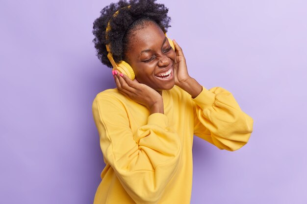 женщина слушает музыку в наушниках, одетая в желтый джемпер на фиолетовом фоне