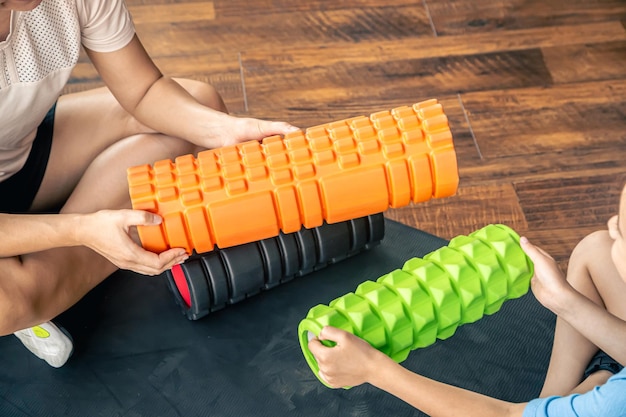 Free photo woman and little girl holding foam rollers sitting on the gym mat