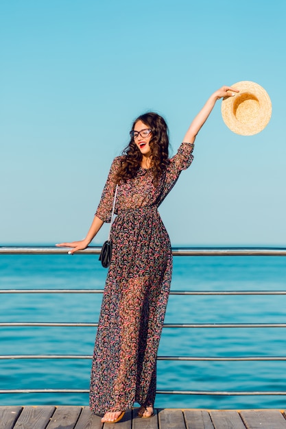 woman in long dress and straw hat having fun by the sea