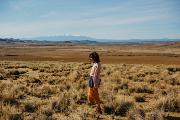 長袖のセーターと乾いた草で大きな茶色の野原に立っているロングスカートの女性