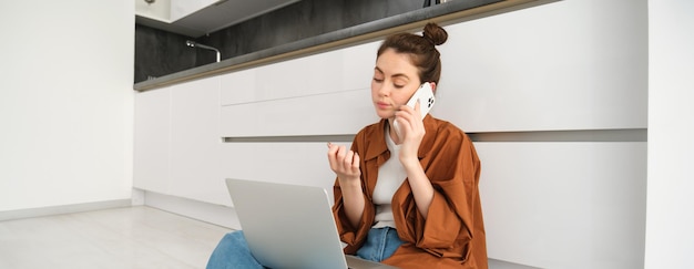 Foto gratuita una donna che sembra annoiata e non divertita mentre è seduta sul pavimento e ascolta una conversazione ha il portatile acceso