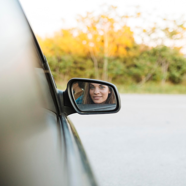 Женщина смотрит в зеркало автомобиля, находясь в машине