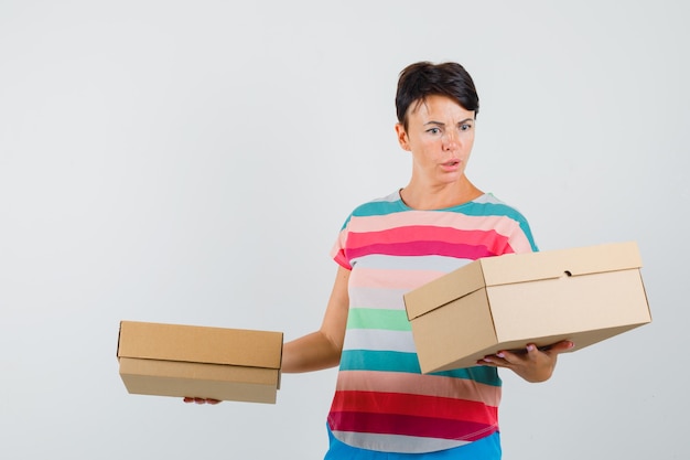 Woman looking at cardboard boxes in striped t-shirt and looking confused.