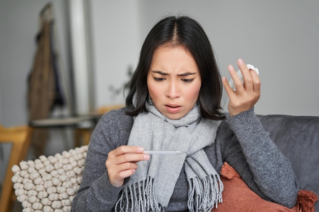 Free photo woman looking concerned and shocked at thermometer catching cold feeling unwell with fever and covid