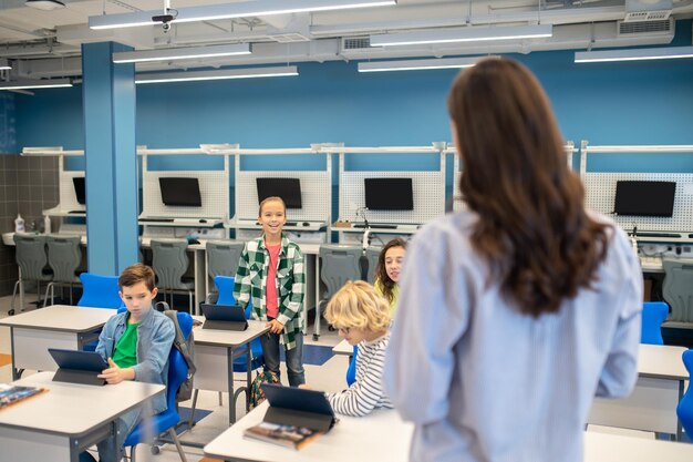 Woman looking at girl answering standing near desk