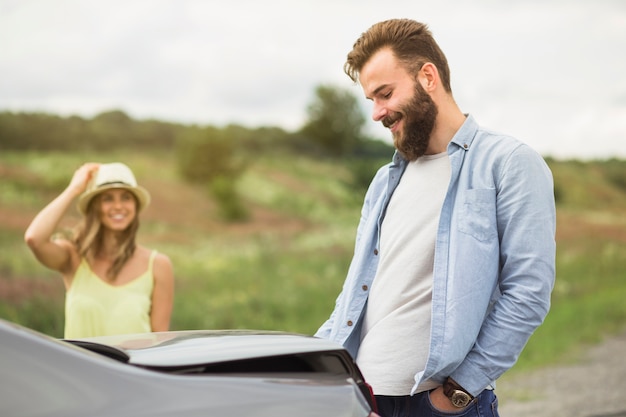 Donna che esamina uomo bello che sta vicino all'automobile all'aperto