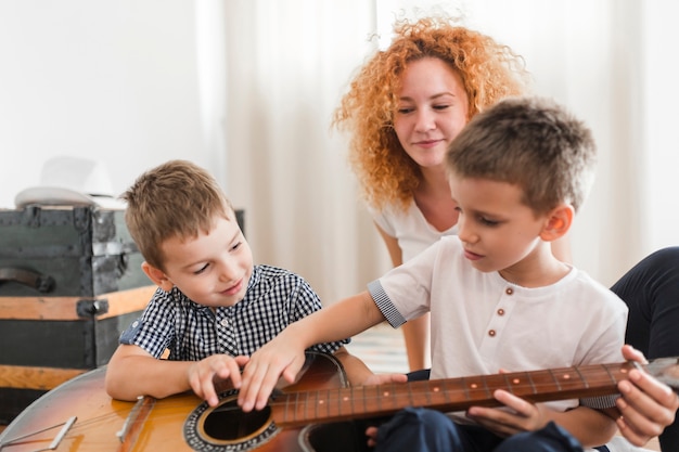 Женщина, глядя на своих детей, играющих на гитаре