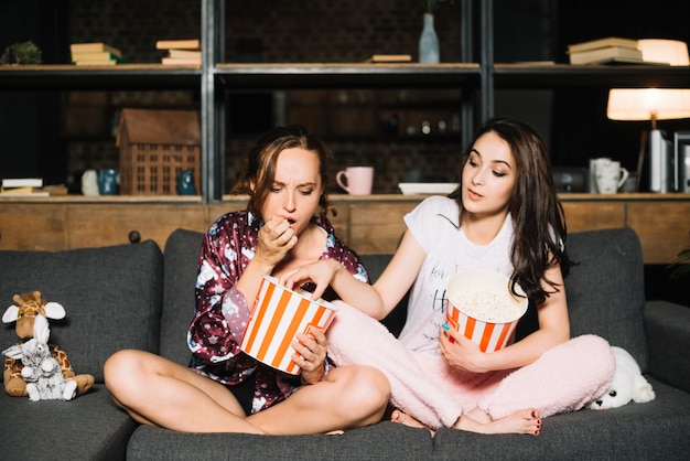 Woman looking at her friend taking popcorn from her bucket