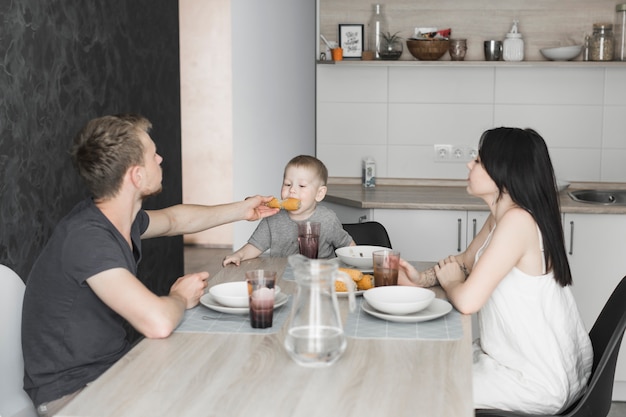 Foto gratuita donna guardando suo marito che alimenta mais al loro figlio