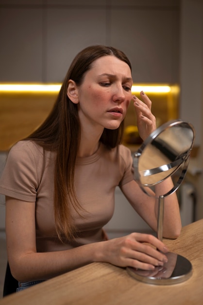 Free photo woman looking at her rosacea in the mirror