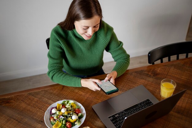 Free photo woman looking at her smartphone while eating her meal