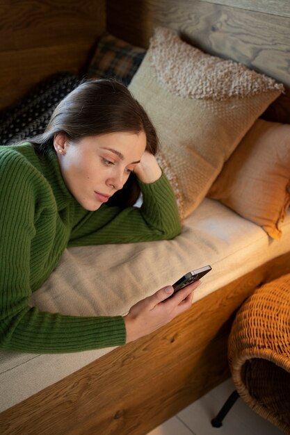 ベッドに横になってスマートフォンを見ている女性