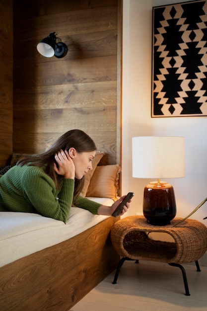 Free photo woman looking at her smartphone while laying on the bed