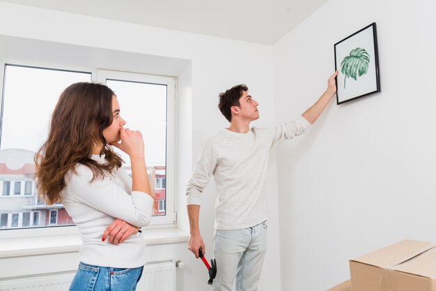 Woman looking at his boyfriend hanging the picture frame on white wall