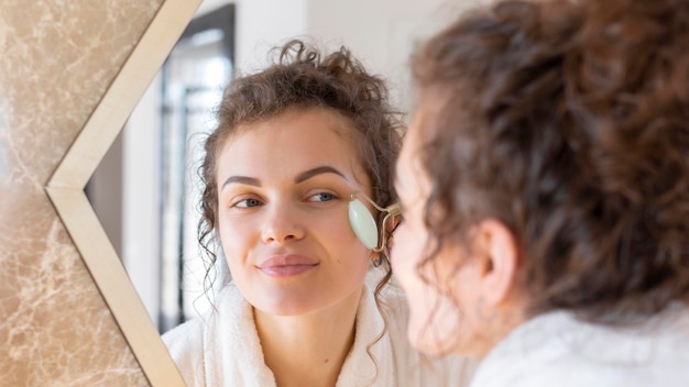 Бесплатное фото Женщина смотрит в зеркало и делает массаж лица