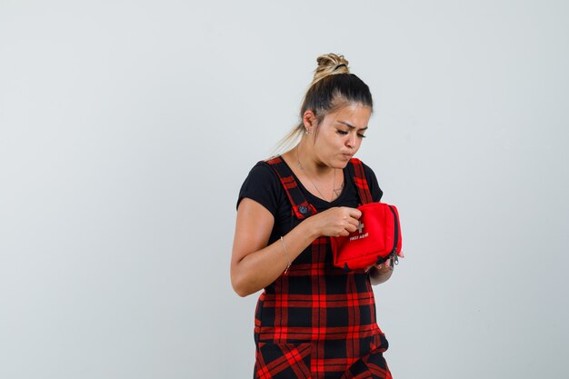 Free photo woman looking into first aid kit in pinafore dress and looking curious , front view.