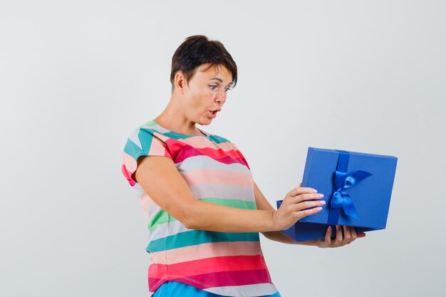 Женщина смотрит в подарочную коробку в полосатой футболке и выглядит изумленной.