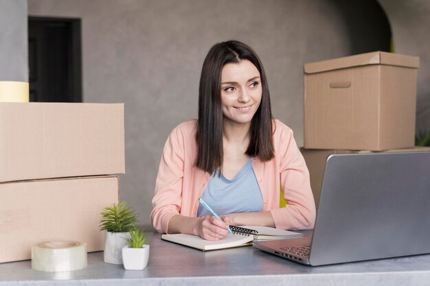 Woman looking at laptop and writing down orders to deliver