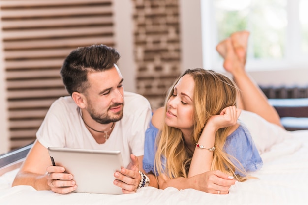 Woman looking at man holding digital tablet on bed