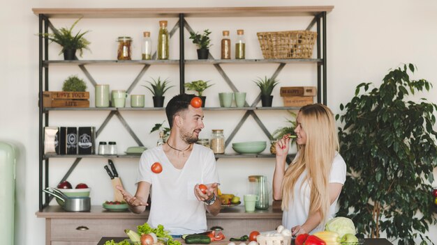 Woman looking at man juggling red tomatoes in the kitchen