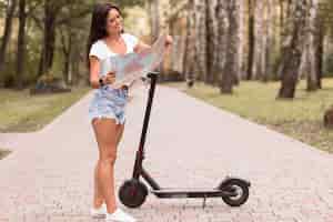Foto gratuita donna che guarda la mappa accanto allo scooter elettrico