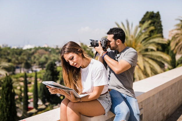 公園のカメラで写真を撮っている彼女のボーイフレンドと一緒に座っている地図を見ている女性