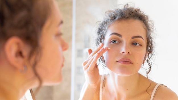 Woman looking in mirror and applying cream on face