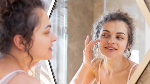 鏡を見て、顔にクリームを塗る女性