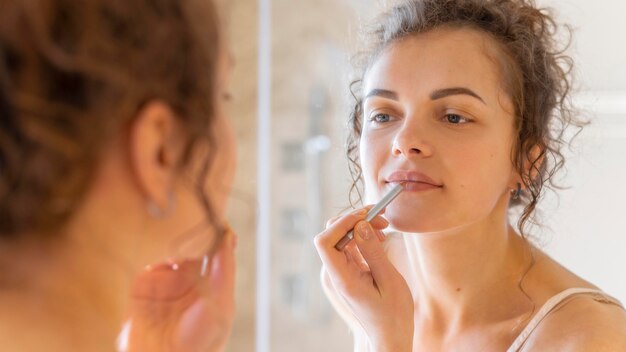 Woman looking in mirror and applying lipstick