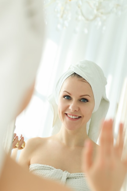 Женщина смотрит в зеркало с полотенцем на голове после душа