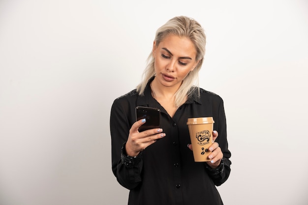 Donna che osserva sul telefono cellulare e che tiene una tazza di caffè. foto di alta qualità