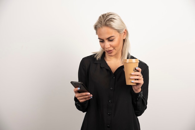 Женщина смотрит на мобильный телефон и держит чашку кофе. Фото высокого качества
