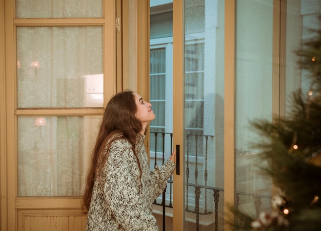 Foto gratuita donna che osserva dalla finestra vicino all'albero di natale