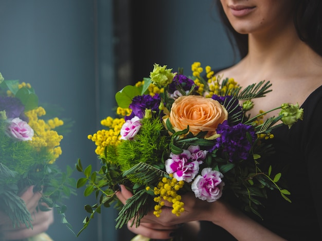 A woman looking to a pretty colorful bouquet of flowers in front of the window