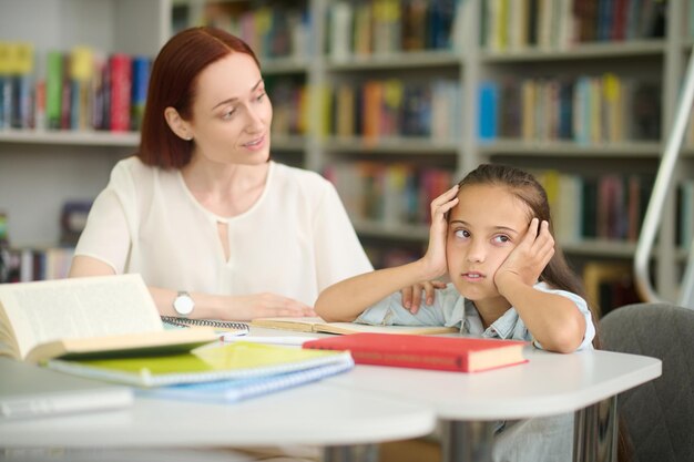 テーブルで勉強している疲れた女の子を疑わしく見ている女性