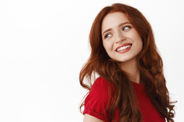 woman, looking behind shoulder carefree, smiling and gazing with thoughtful romantic smile, standing in t-shirt on white