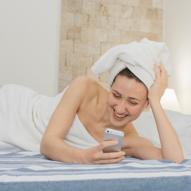 Женщина смотрит на смартфон в постели после душа
