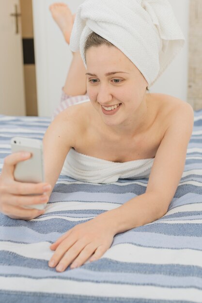 Woman looking at smartphone in bed after shower