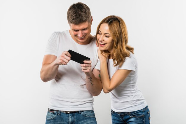 Woman looking at smiling man playing video game on mobile phone against white backdrop