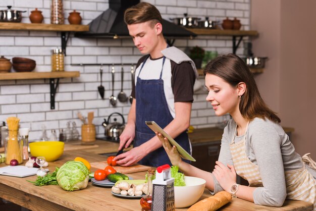 Woman looking at tablet while man cutting tomato