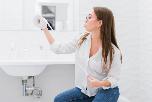 Woman looking at a toilet paper while sitting on the toilet