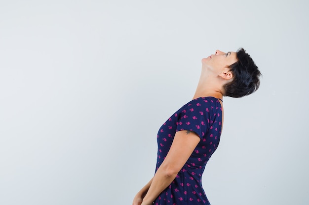 Woman looking upward while bending head back in dress and looking focused .