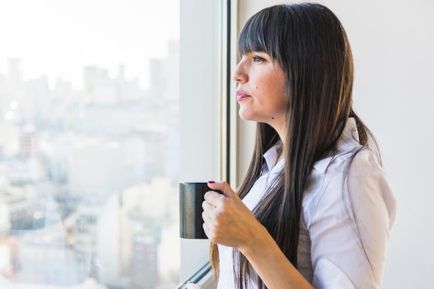 Woman looking at window holding cup of coffee cup