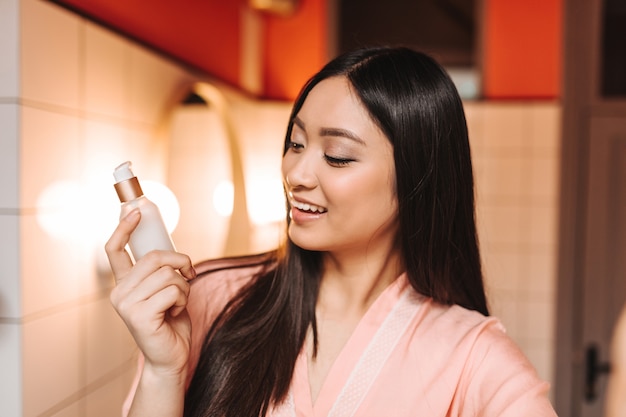 woman looks at face cream with smile and poses in bathroom