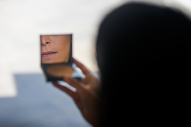 Woman looks in little mirror of her powder