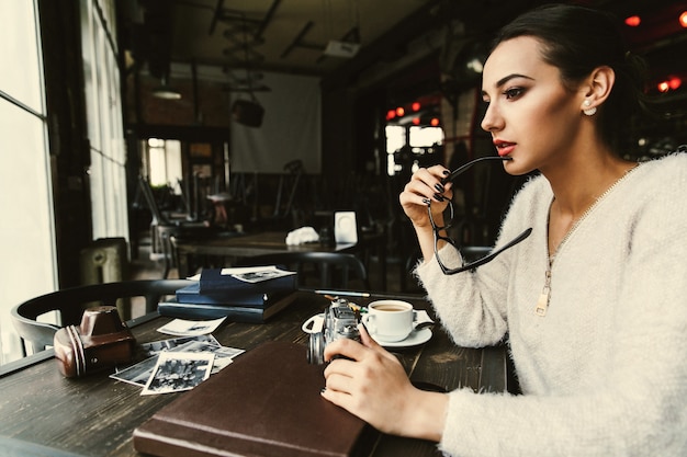 Бесплатное фото Женщина выглядит задумчиво сидит за столом со старыми фотографиями в кафе