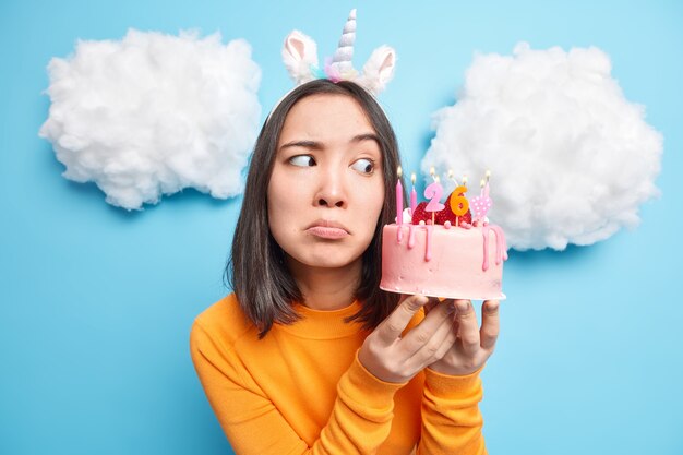 woman looks with temptation at delicious strawberry cake wears unicorn headband orange jumper celebrates birthday poes on blue 