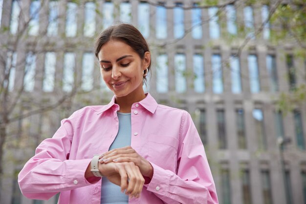 woman looks at wrist watch comes on date with boyfriend being late checks time poses outdoors against city building