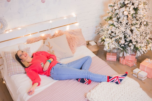Woman lying on bed next to christmas tree
